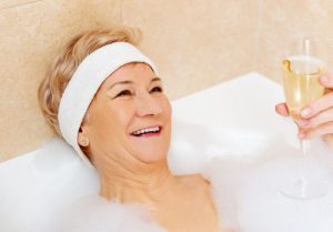 Gut gelaunte Seniorin mit Sekt in Badewanne
